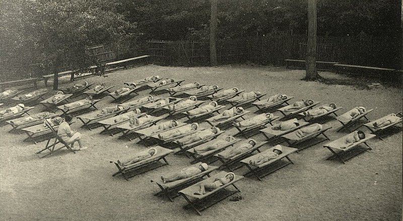 Cots lined up in a sunny area, with children resting in the sun.